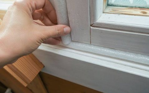 Foam weatherstripping being pressed into a window frame to stop drafts